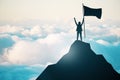 An individual with an outstretched arm holds a flag on the summit of a mountain above the clouds, denoting success Royalty Free Stock Photo