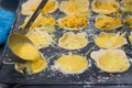 Individual quiches being made for breakfast, ladle pouring egg into filled pastry shells in muffin tin