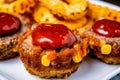 Individual servings of mini meatloaf topped with tangy BBQ sauce, served with crispy onion rings and sweet corn