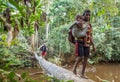Woman with child crossing river on the tree trunk bridge, tribe of Korowai people.