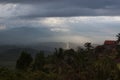 Indonesian landscape with rainy sky, dark blue clouds, sunbeams over hazy shining hills, mountains, green valley with tropical.