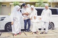 Indonesian muslim multi-generation family standing next to a car