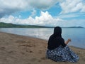 Indonesian Muslim Woman Sitting, Relaxing, and Enjoying the Beautiful View of the Beach During Summer Royalty Free Stock Photo