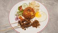 Indonesian Nasi Goreng with Satay, Fried Egg, Pickles, and Crackers on Marble Table