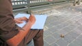 Indonesian security guard sitting holding a pen and book to write visitor data in the guest book outside the guard post