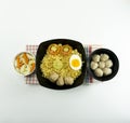 Indonesian Warm noodles served with eggs and fresh tomatoes with meatballs on a black bowl and pickled on a white bowl on a white