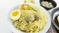 Indonesian Warm noodles served with fresh tomatoes and meatballs on a white round bowl and pickles on a white bowl on a white