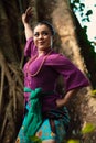 An Indonesian woman bravely poses while raising her hands in a purple dress