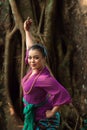 An Indonesian woman bravely poses while raising her hands in a purple dress