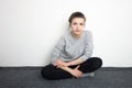 Indoor close up portrait of charming young lady of European appearance wearing grey sweatshirt, black jeans sitting grey carpet ag