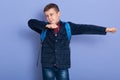 Indoor image of adorable playful little boy raising arms, closing one eye, wearing jeans, plaid shirt and jacket, studying hard, Royalty Free Stock Photo