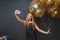 Indoor photo of romantic fair-haired birthday girl making selfie on dark background. Smiling curly caucasian woman