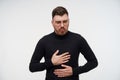 Indoor photo of young bearded brunette man with short haircut holding palms on his stomach and grimacing his face, feeling sick