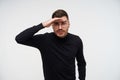 Indoor photo of young handsome bearded brunette man squinting his eyes and keeping forefinger on forehead while looking ahead, Royalty Free Stock Photo