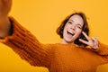 Indoor portrait of blissful girl in knitted clothes making selfie and laughing on bright background. Enchanting young