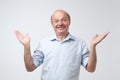 Indoor portrait of confused senior man in yellow t-shirt showing I have no idea gesture Royalty Free Stock Photo