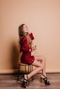 Indoor portrait of glamorous woman in black sandals and party dress sitting on chair on beige background. Shapely cute Royalty Free Stock Photo