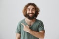 Indoor portrait of handsome kind arabian man with curly hair and beard smiling broadly while pointing left or behind