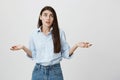 Indoor portrait of hesitant woman with questioned expression, lifting hands in weighing gesture, looking up while