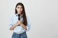 Indoor portrait of perplexed and questioned young woman, holding microphone while thinking and looking aside, standing