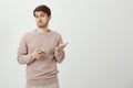 Indoor portrait of puzzled and clueless young man gesturing and shrugging while holding smartphone and looking confused Royalty Free Stock Photo