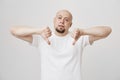 Indoor portrait of unhappy bothered bald caucasian man with beard showing thumbs down and being unimpressed, standing