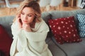 indoor portrait of young selfish beautiful woman enjoying winter time at home, sitting on cozy couch in warm sweater