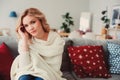 indoor portrait of young selfish beautiful woman enjoying winter time at home, sitting on cozy couch in warm sweater