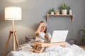 Indoor shor of sick ill woman wearing sleeping mask holding laptop while lying on bed, using cell phone to call to doctor, having