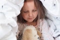 Indoor shot of adorable little child girl playing with teddy bear in bed under blanket, charming kid plays in morning before Royalty Free Stock Photo