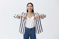 Indoor shot of amazed carefree beautiful woman in striped blouse and jeans, laughing out loud from happiness, pointing Royalty Free Stock Photo