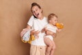 Indoor shot of amazed excited joyful mother with her baby standing and talking on mobile phone, hearing good news, spending Royalty Free Stock Photo