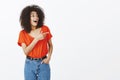 Indoor shot of amazed happy outgoing woman with dark skin and curly hair, pointing and looking right with pleased