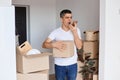 Indoor shot of angry aggressive handsome man wearing white t shirt standing with cardboard box, holding cell phone and screaming Royalty Free Stock Photo