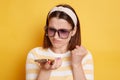 Indoor shot of angry woman wearing striped t shirt, hair band and sunglasses, using cell phone and with hate, clenched fist with