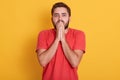 Indoor shot of astonished bearded male, keeping ands on mouth, being stunned by bad news, posing against yellow concrete