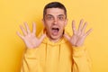 Indoor shot of astonished scared brunette man wearing casual style hoodie, looking at camera with big eyes, open mouth and raised Royalty Free Stock Photo