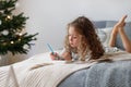 Indoor shot of attentive pretty small girl writes letter to Santa Claus before Christmas, thinks what present she Royalty Free Stock Photo