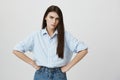 Indoor shot of attractive angry wife, standing with hands on waist and showing blaming look at camera, standing over