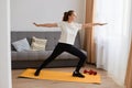 Indoor shot of attractive Caucasian young woman practicing yoga on exercise mat in living room while resting at home, working out Royalty Free Stock Photo