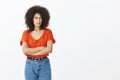 Indoor shot of attractive female social outcast with afro hairstyle, frowning, holding hands crossed on chest, staring