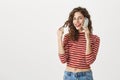 Indoor shot of attractive slender female with curly hairstyle and red lipstick talking on smartphone, touching curl Royalty Free Stock Photo