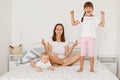 Indoor shot of attractive sporty woman sitting in lotus pose and trying meditating on bed with her children, elder girl yelling Royalty Free Stock Photo