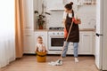 Indoor shot of attractive woman making domestic work and taking care of her infant baby, wiping washing floor in kitchen, looking Royalty Free Stock Photo