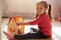 Indoor shot of baby girl playing with doll housewhile sitting at home during coronavirus quarantine, child sitting on floor and Royalty Free Stock Photo