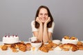 Indoor shot of beautiful delighted caucasian woman with brown hair sitting at table isolated over gray background, keeps hands