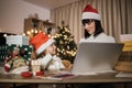 Happy young woman and her girl shopping online on laptop in cozy Christmas interior Royalty Free Stock Photo