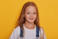 Indoor shot of beautiful little girl with long blonde hair posing isolated over yellow background, looking at camera, charming kid Royalty Free Stock Photo