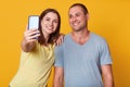 Indoor shot of beautiful young couple looking at camera of cell phone, make selfie portrait, wearing gray and yellow t shirts, Royalty Free Stock Photo