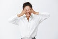 Indoor shot of charming carefree african-american female employer with white shirt, covering eyes with palms, being Royalty Free Stock Photo